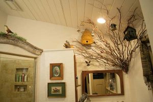 Elaine refers to the master bath as “the bird bath,” due to its bird-related décor. Kerry Kegerise helped her design the “tree” that grows out of one of the walls. Birds and birdhouses decorate it. She found the wooden arch that tops the shower door at a “junk place” along Route 322 and put it to use.